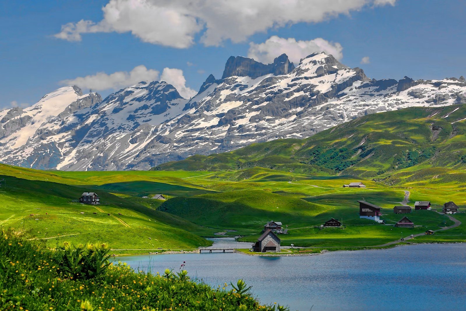 Alpine lake and pastures beneath snow-covered Swiss peaks